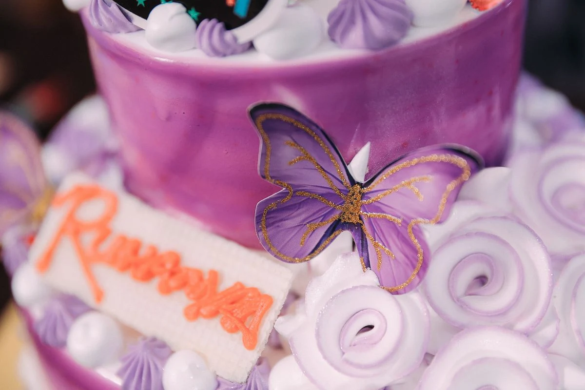 Representative celebration cake with purple piped frosting and butterfly decorations