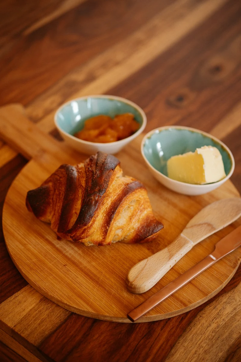 Representative golden croissant beside butter and jam