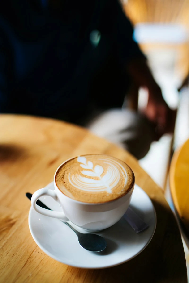 Representative milk coffee with leaf-shaped foam art in a ceramic cup and saucer